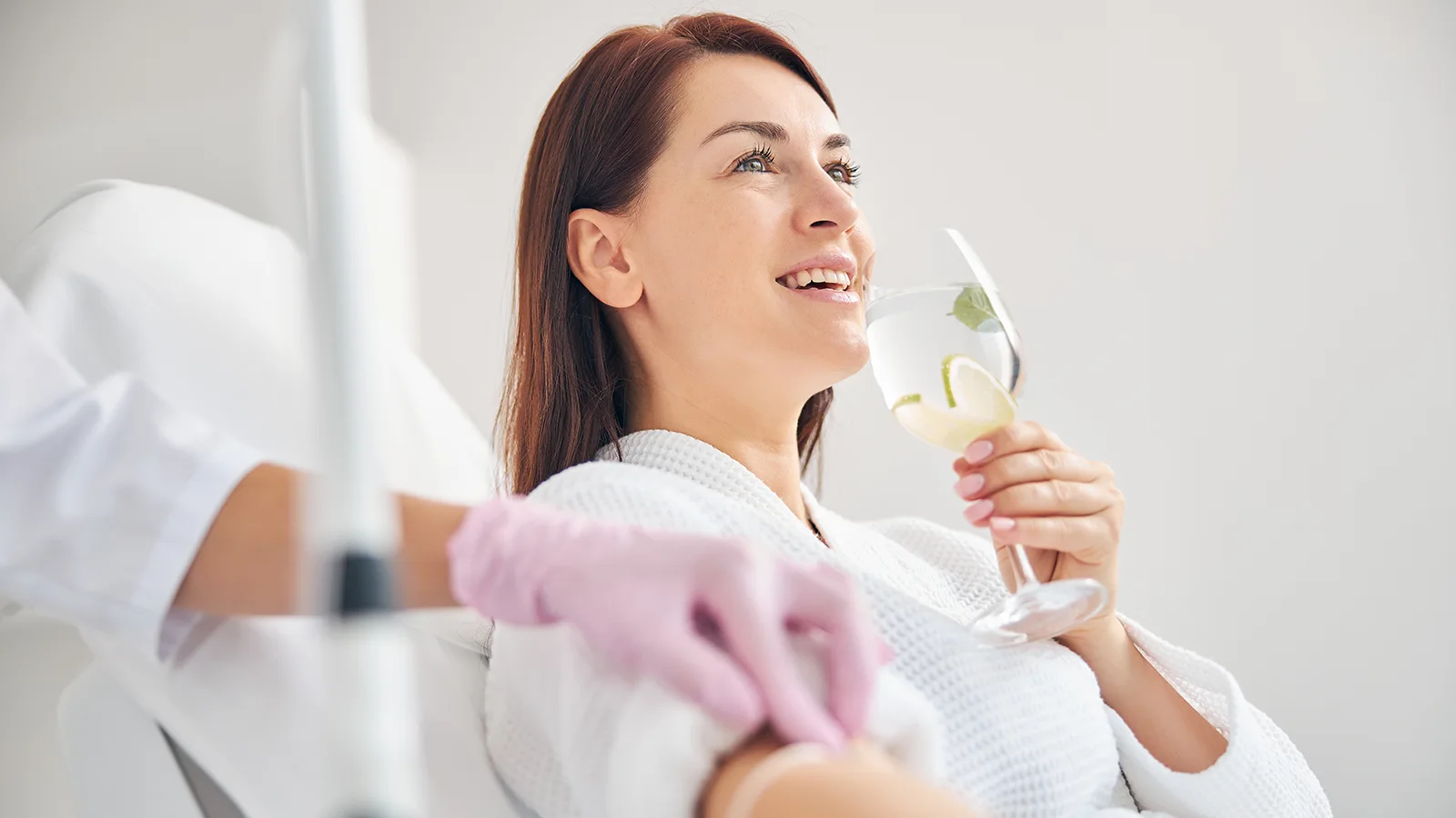 woman receiving IV hydration and drinking glass of water